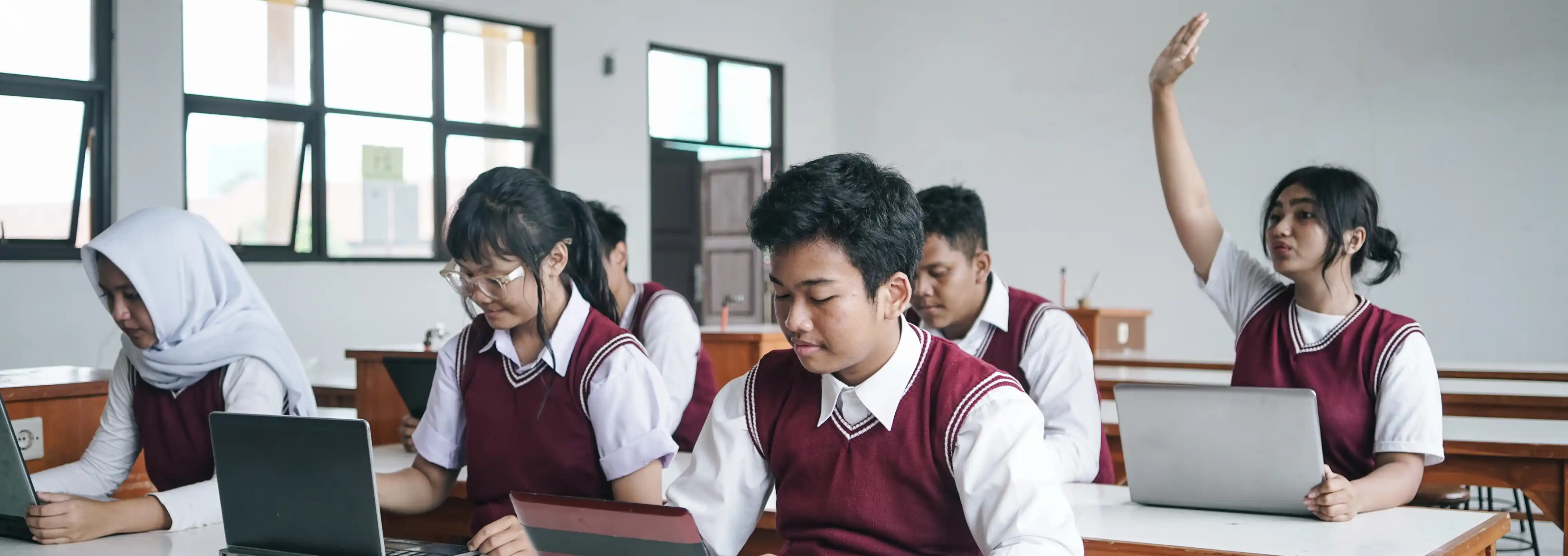 Focused students learning from laptop, one student with hand raised